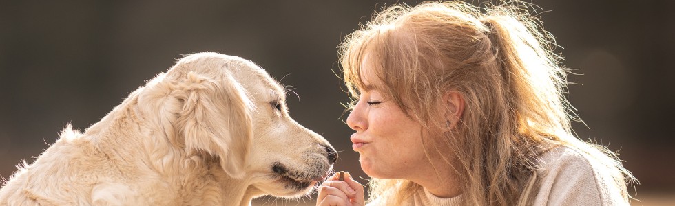 vrouw met hondensnack in haar hand kijkt hond heel lief aan